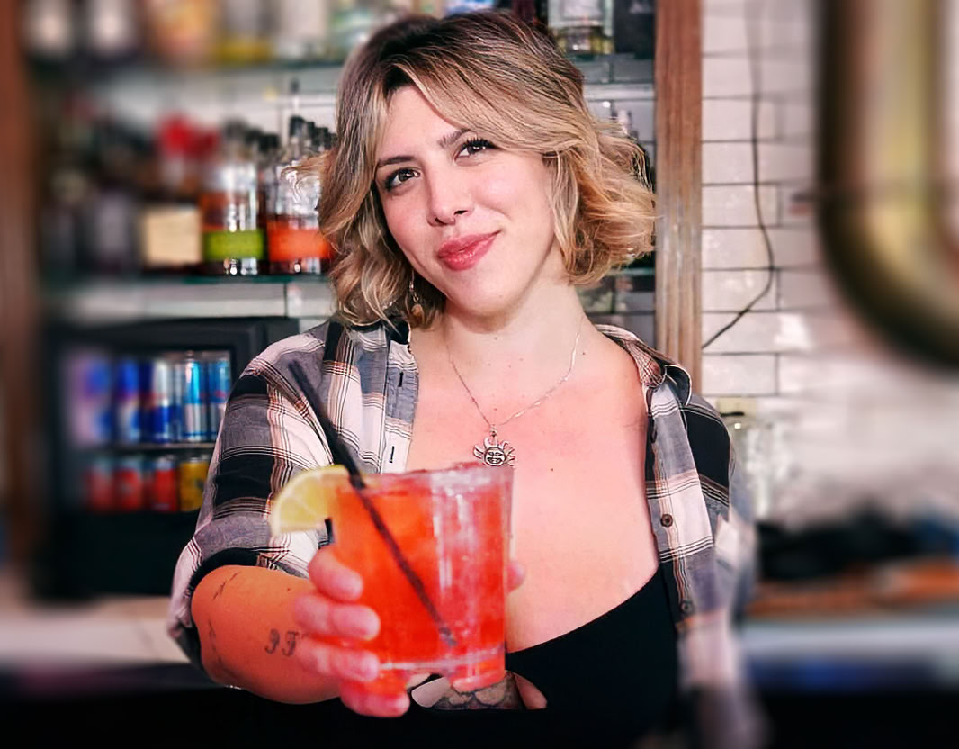 A bartender carefully adds a garnish to a cocktail using tweezers at a bar counter.